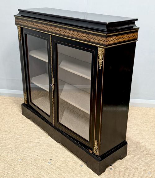 fig 1. A black ebonised two-door glazed cabinet featuring a moulded caddy top, brass ormolu corner mounts, and a band of geometric marquetry inlay.