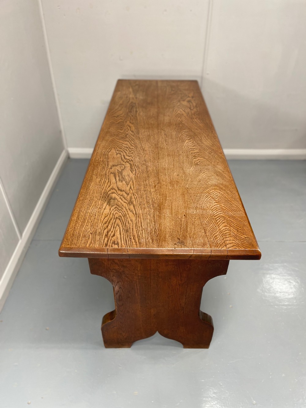 A long, solid oak altar table featuring a smooth rectangular top surface resting on two shaped slab end legs. View IX