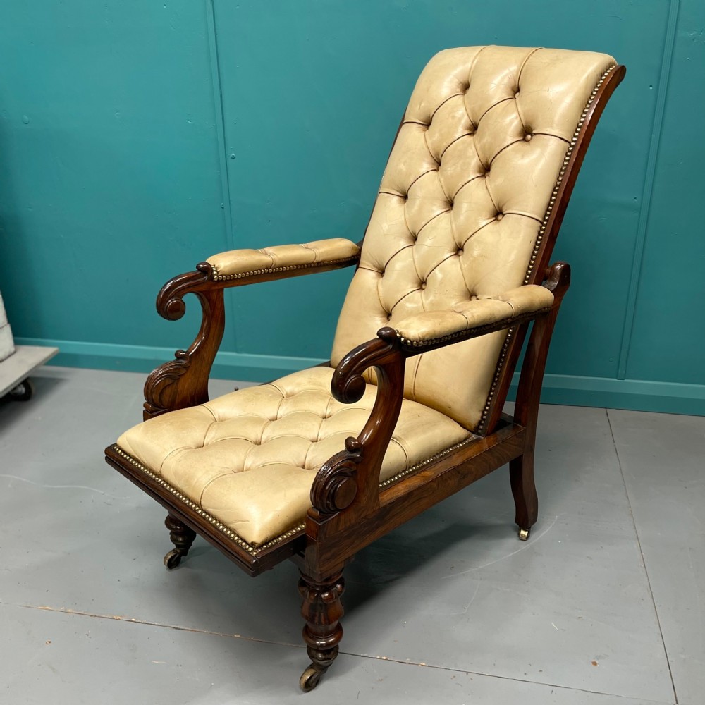 A Late Regency mahogany reclining armchair featuring buttoned tan leather upholstery, brass stud trim, scroll arms, and turned front legs on castors.