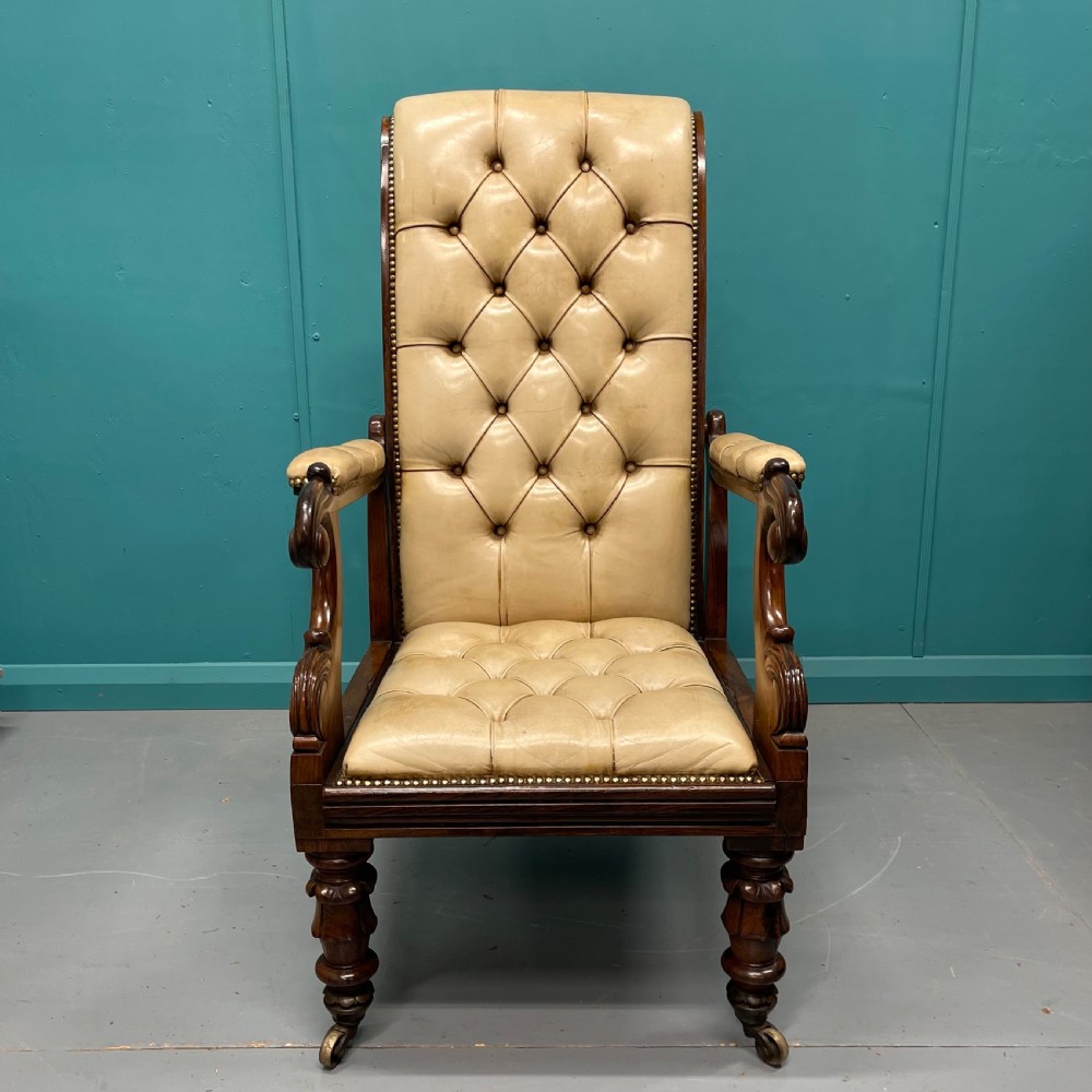A Late Regency mahogany reclining armchair featuring buttoned tan leather upholstery, brass stud trim, scroll arms, and turned front legs on castors. View III