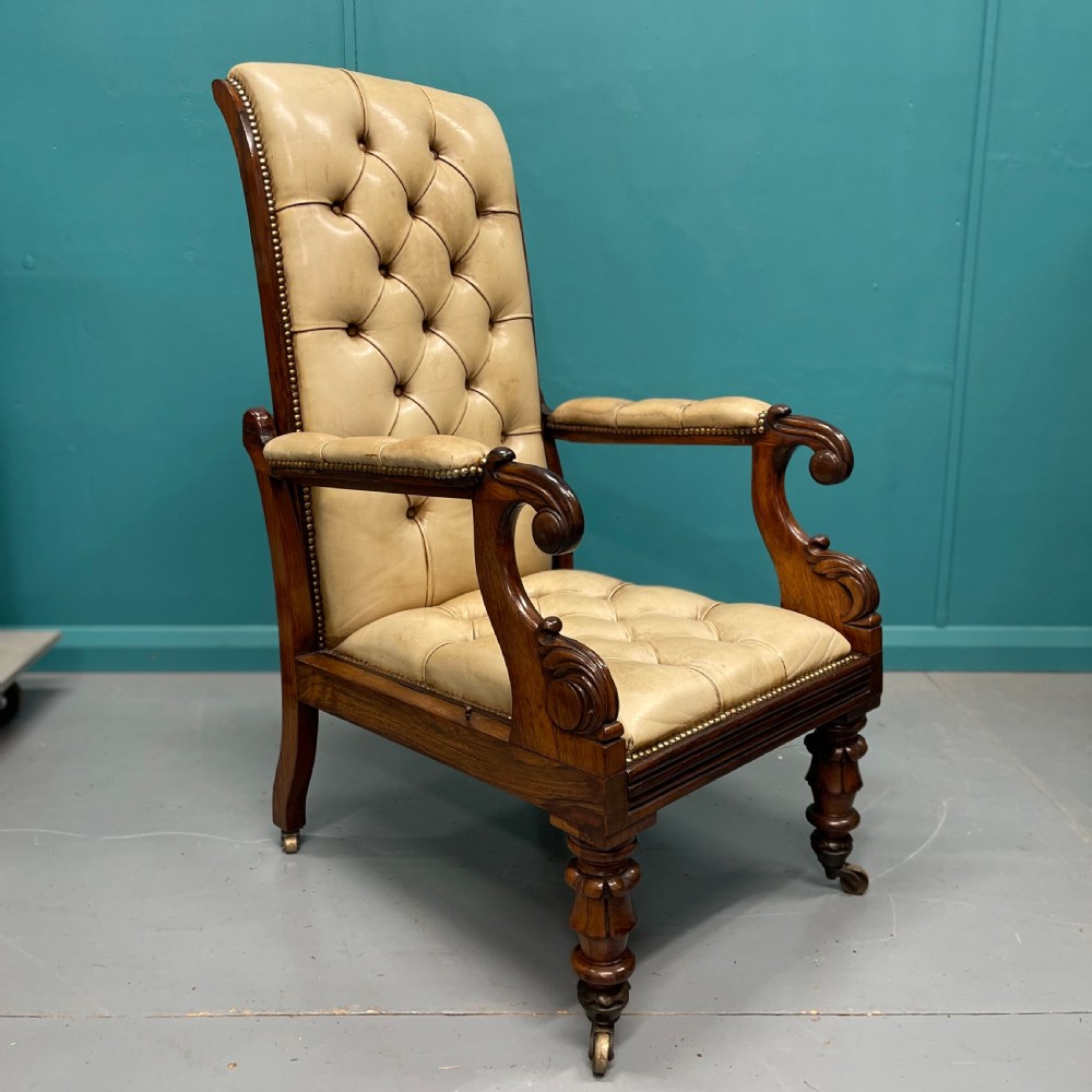 A Late Regency mahogany reclining armchair featuring buttoned tan leather upholstery, brass stud trim, scroll arms, and turned front legs on castors. View V