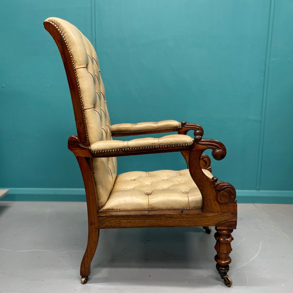 A Late Regency mahogany reclining armchair featuring buttoned tan leather upholstery, brass stud trim, scroll arms, and turned front legs on castors. View VI