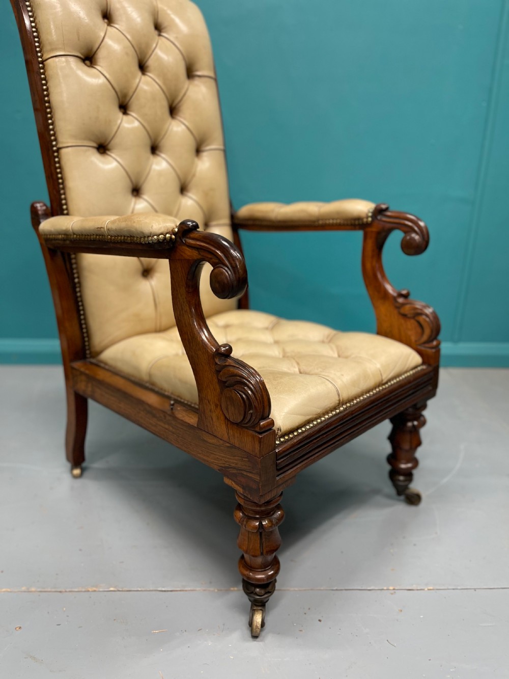 A Late Regency mahogany reclining armchair featuring buttoned tan leather upholstery, brass stud trim, scroll arms, and turned front legs on castors. View VII