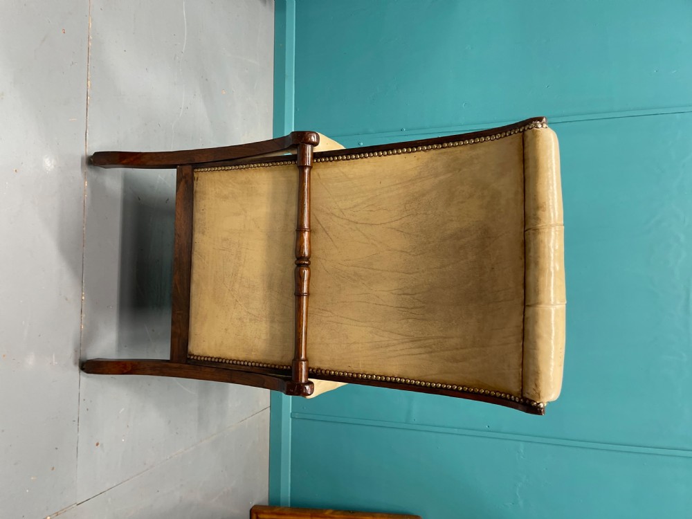 A Late Regency mahogany reclining armchair featuring buttoned tan leather upholstery, brass stud trim, scroll arms, and turned front legs on castors. View IX