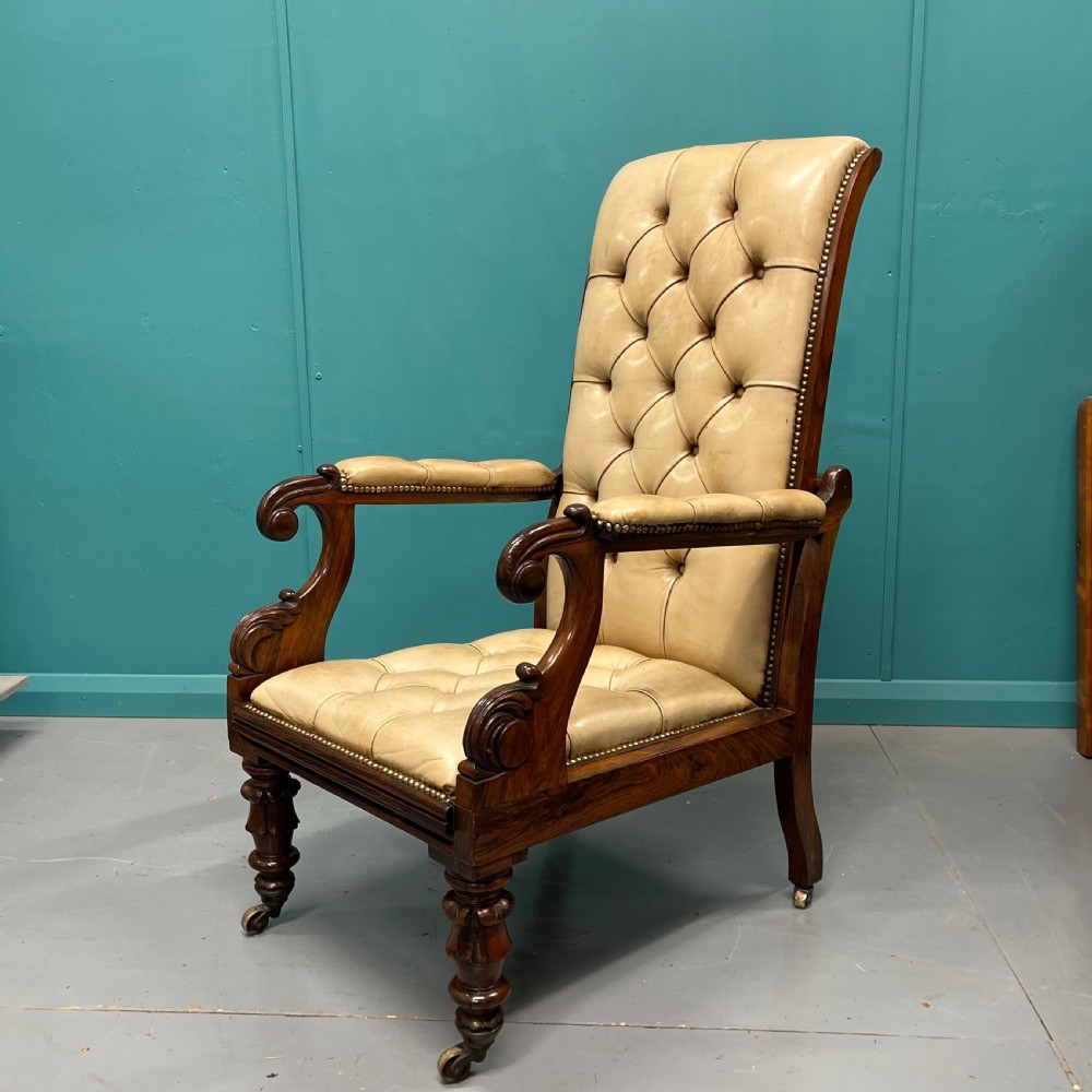 A Late Regency mahogany reclining armchair featuring buttoned tan leather upholstery, brass stud trim, scroll arms, and turned front legs on castors. View X