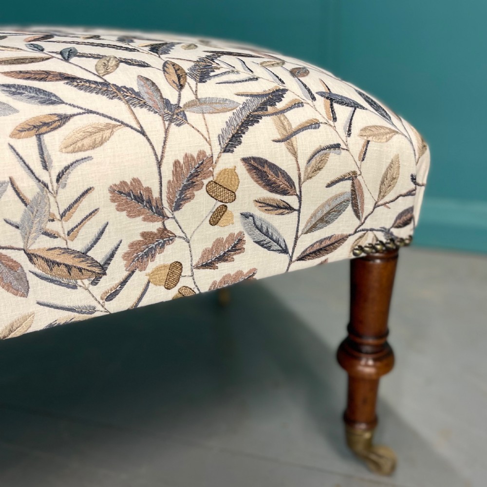 Newly upholstered leaf motif footstool on castors View III