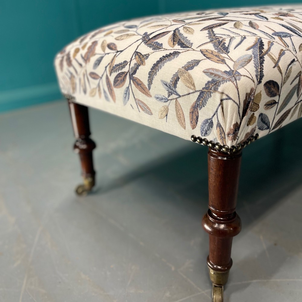Newly upholstered leaf motif footstool on castors View IV