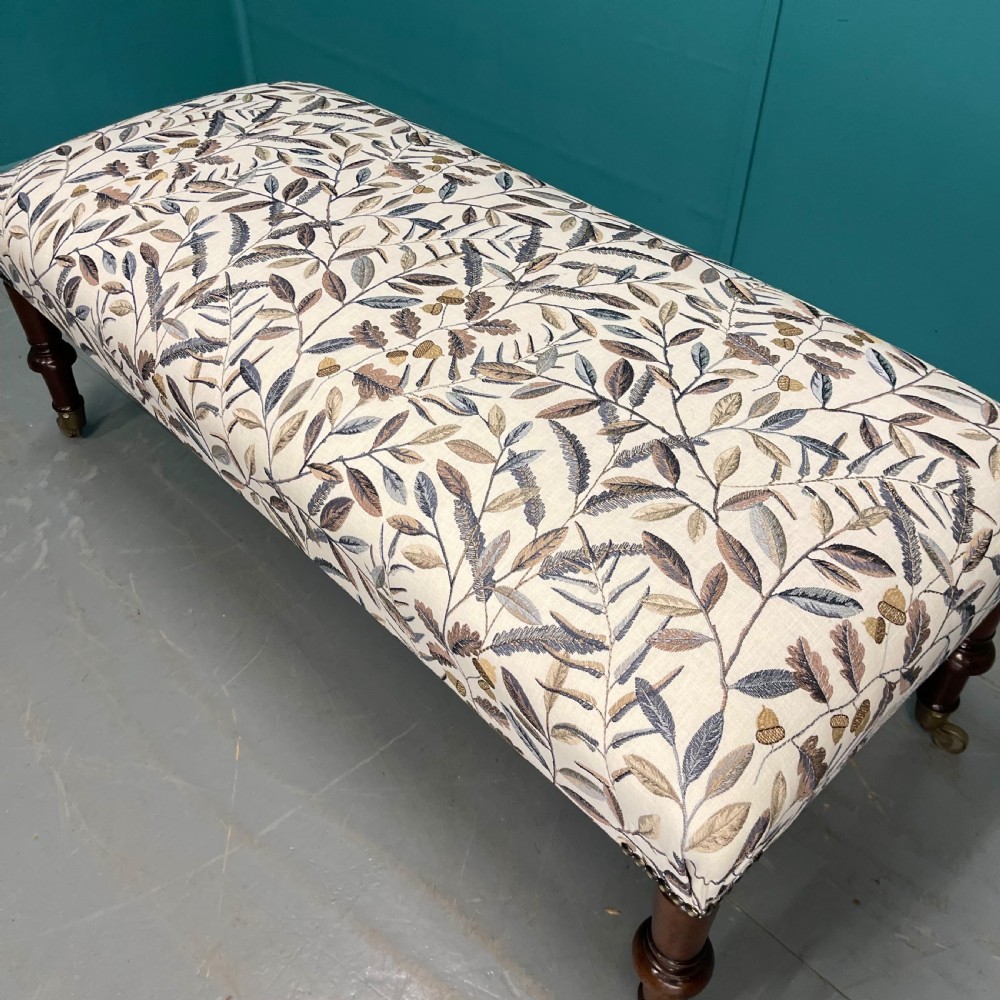 Newly upholstered leaf motif footstool on castors View V