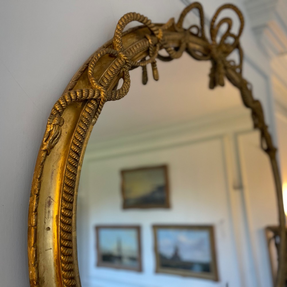 A large French gilt overmantel mirror featuring an oval glass plate surrounded by rope twist mouldings, a ribbon crest, and carved dolphin corner supports. View III