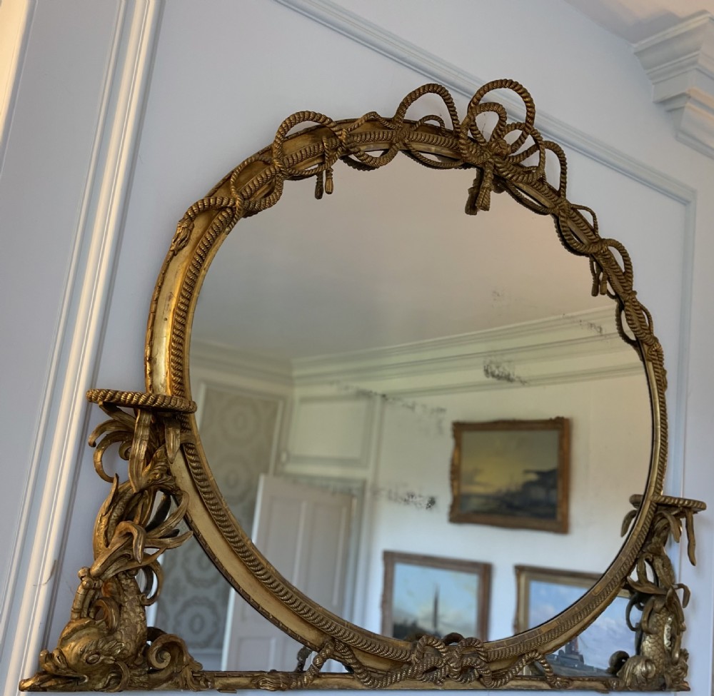 A large French gilt overmantel mirror featuring an oval glass plate surrounded by rope twist mouldings, a ribbon crest, and carved dolphin corner supports. View IV