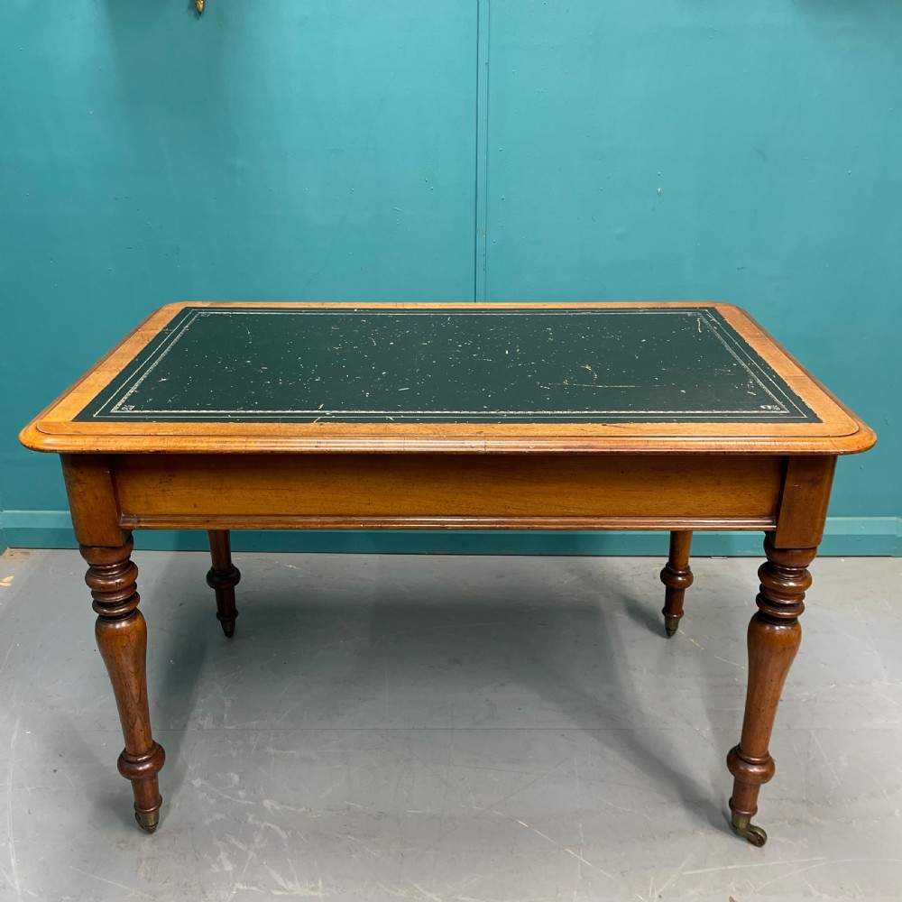A rectangular Victorian timber library table featuring a green leather insert top with gold tooling, turned legs, and brass castors. View V