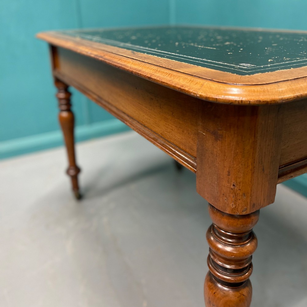 A rectangular Victorian timber library table featuring a green leather insert top with gold tooling, turned legs, and brass castors. View VII
