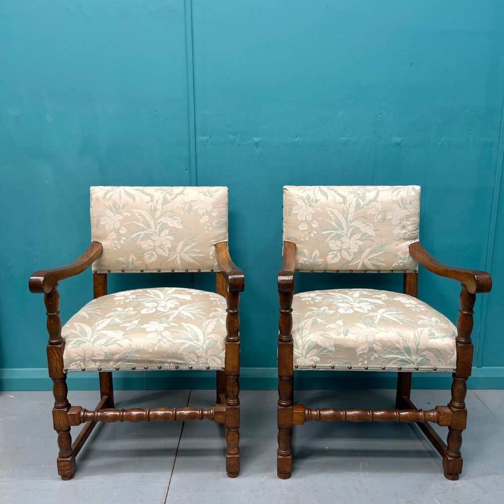 A pair of English oak armchairs featuring turned legs, stretchers, open curved armrests, and floral pattern cream upholstery secured with metal studs. View II