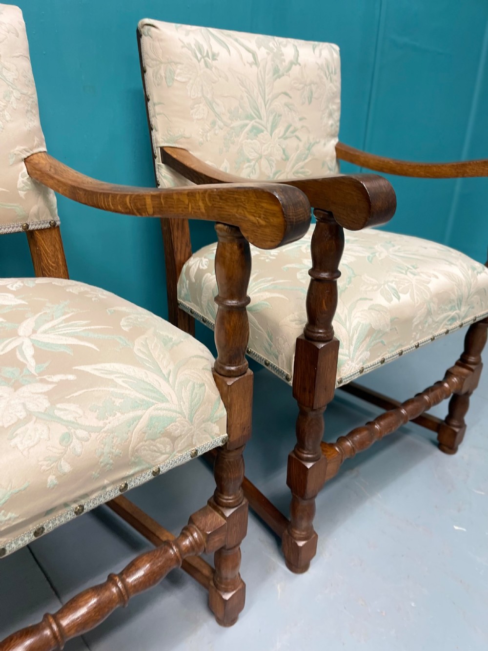 A pair of English oak armchairs featuring turned legs, stretchers, open curved armrests, and floral pattern cream upholstery secured with metal studs. View III