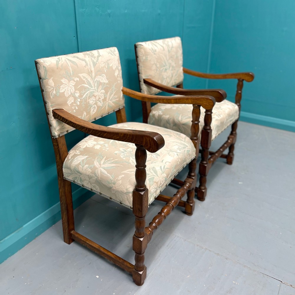 A pair of English oak armchairs featuring turned legs, stretchers, open curved armrests, and floral pattern cream upholstery secured with metal studs. View V