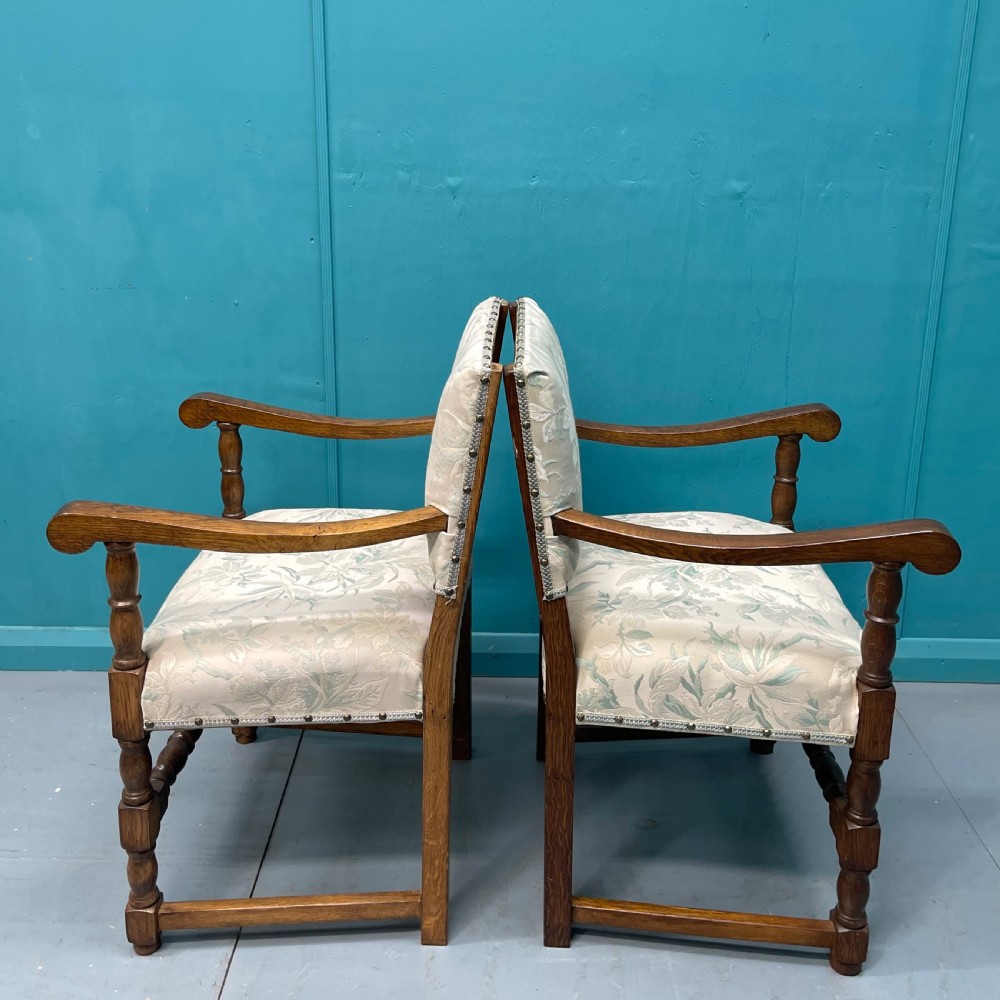 A pair of English oak armchairs featuring turned legs, stretchers, open curved armrests, and floral pattern cream upholstery secured with metal studs. View VI
