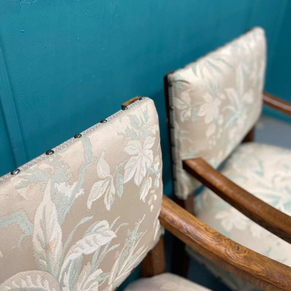 A pair of English oak armchairs featuring turned legs, stretchers, open curved armrests, and floral pattern cream upholstery secured with metal studs. View VII