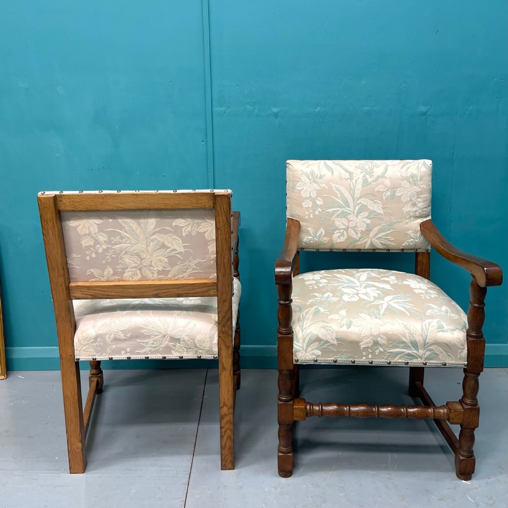 A pair of English oak armchairs featuring turned legs, stretchers, open curved armrests, and floral pattern cream upholstery secured with metal studs. View VIII