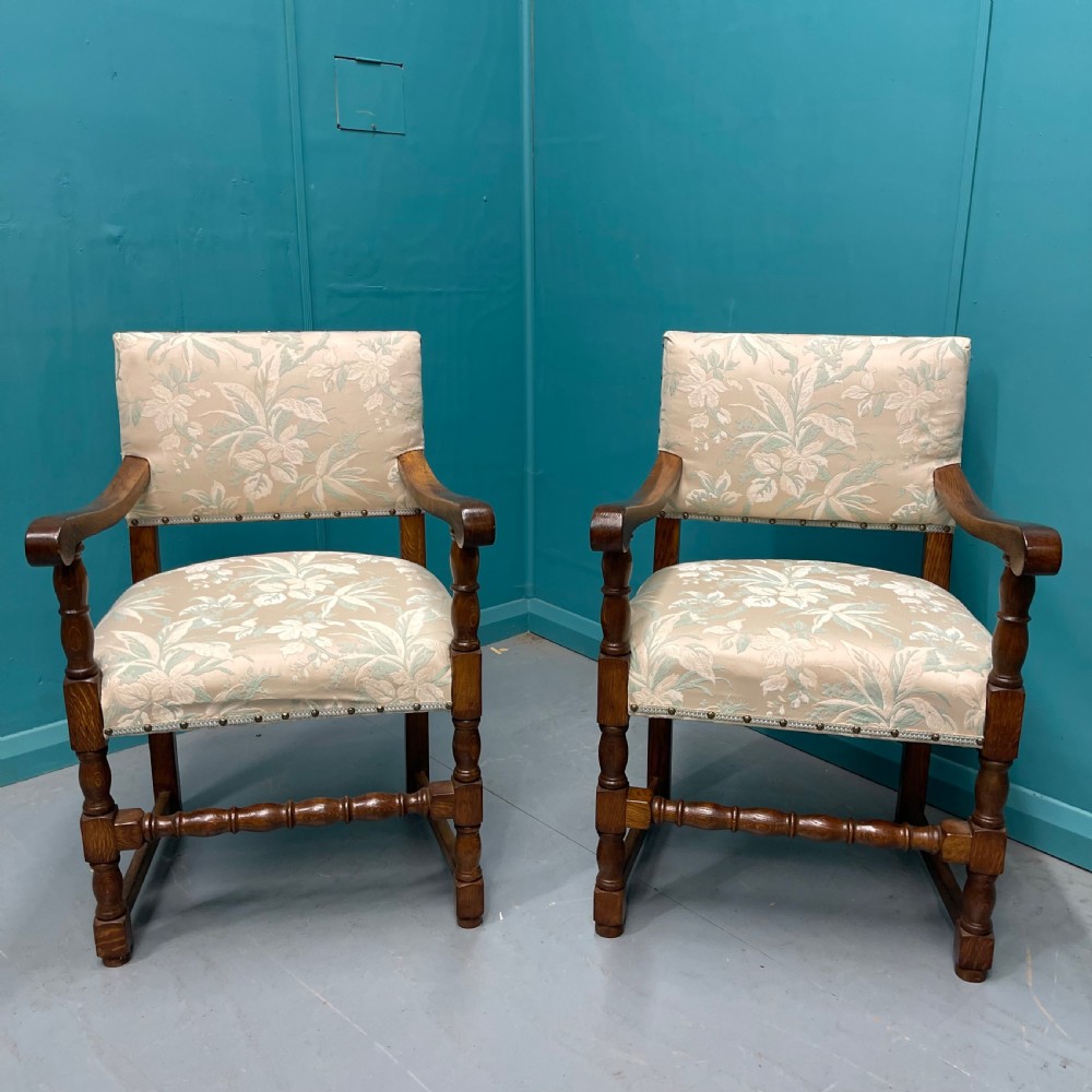 A pair of English oak armchairs featuring turned legs, stretchers, open curved armrests, and floral pattern cream upholstery secured with metal studs. View IX