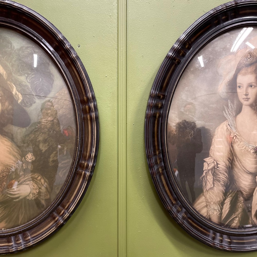 A pair of matching oval portraits featuring 18th-century style figures, housed under convex glass within dark moulded frames. View II