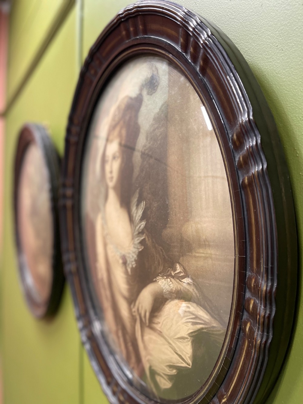 A pair of matching oval portraits featuring 18th-century style figures, housed under convex glass within dark moulded frames. View V