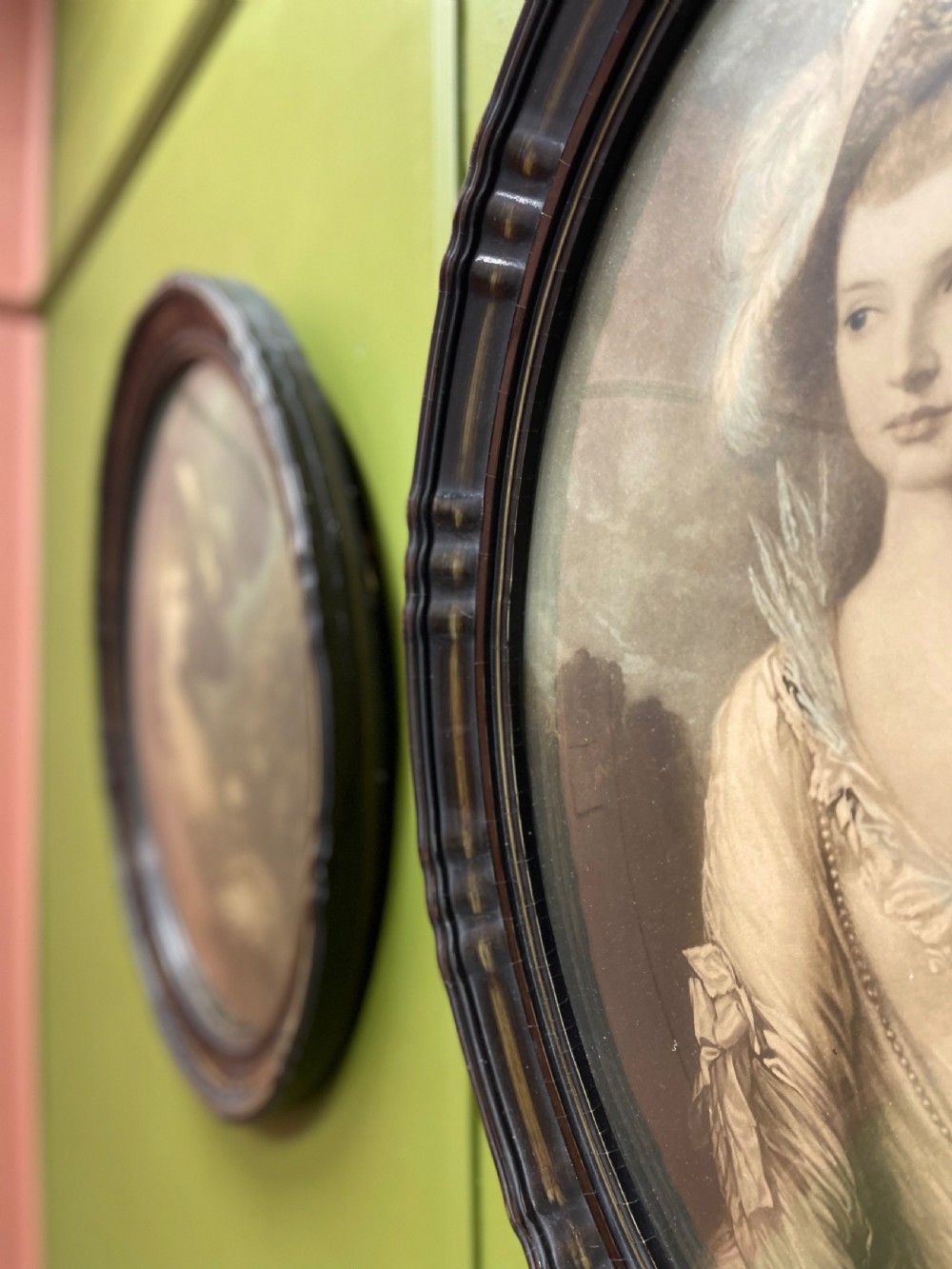 A pair of matching oval portraits featuring 18th-century style figures, housed under convex glass within dark moulded frames. View VI