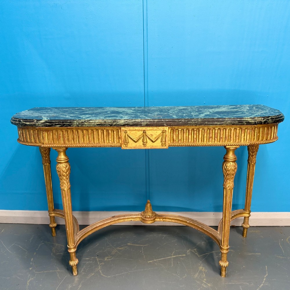 An Adam style giltwood console table featuring a dark green marble top, fluted frieze with swag carvings, and slender tapered legs.
