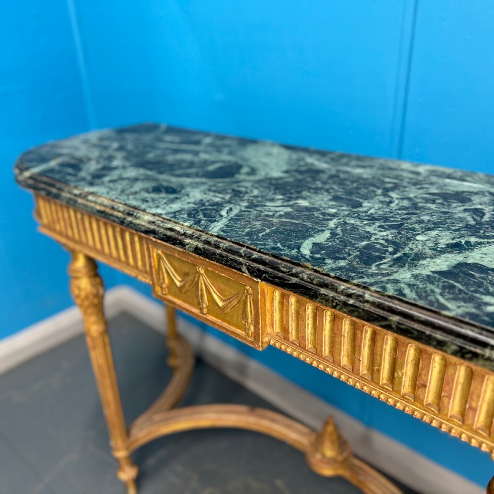 An Adam style giltwood console table featuring a dark green marble top, fluted frieze with swag carvings, and slender tapered legs. View II