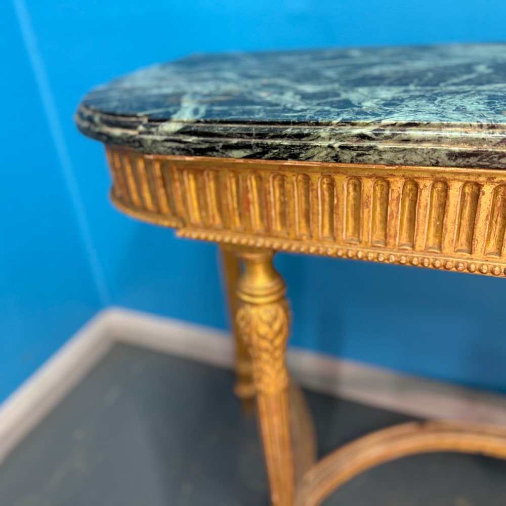 An Adam style giltwood console table featuring a dark green marble top, fluted frieze with swag carvings, and slender tapered legs. View X