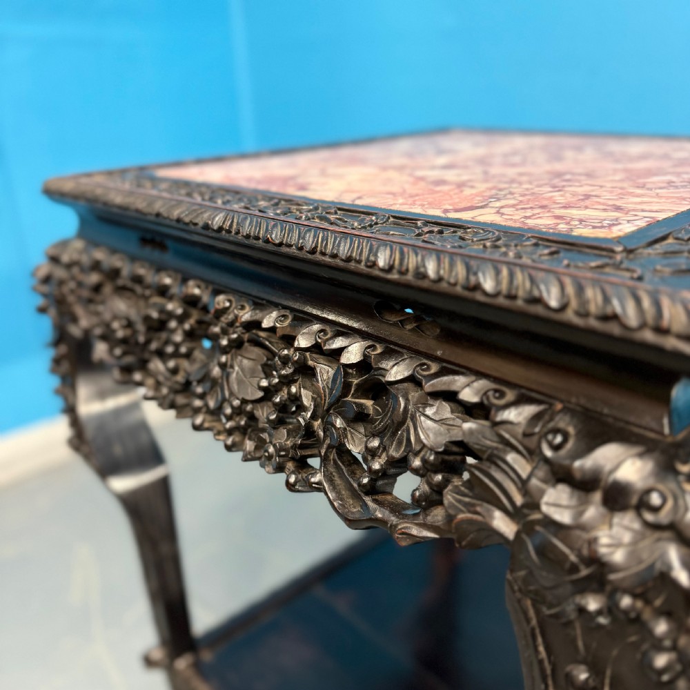 A dark carved Chinese hardwood side table with an inset pink marble top, openwork grapevine apron, cabriole legs, and a lower shelf. View III