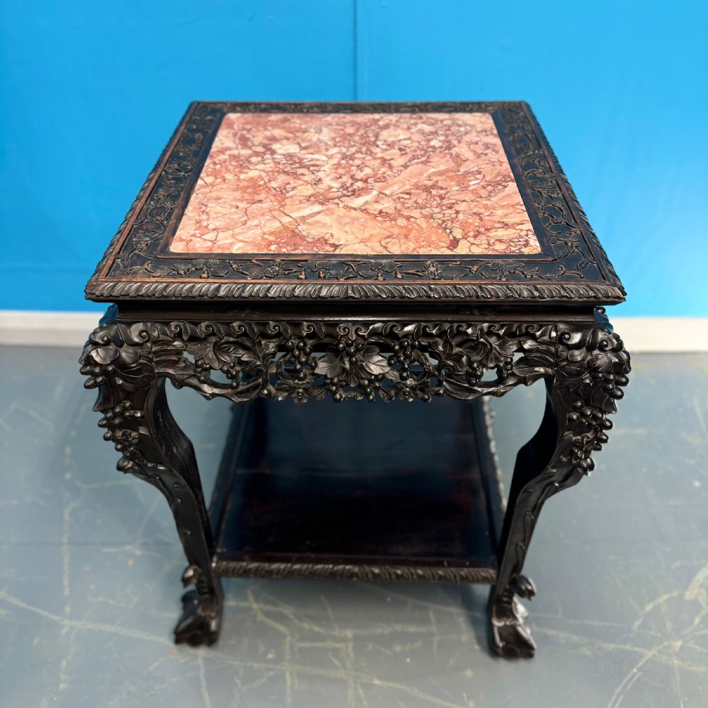 A dark carved Chinese hardwood side table with an inset pink marble top, openwork grapevine apron, cabriole legs, and a lower shelf. View VII