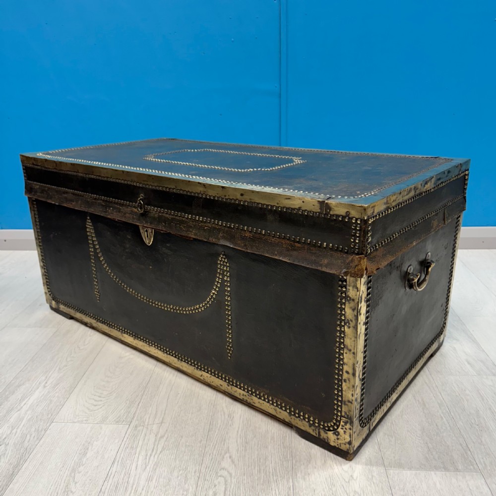 A 19th-century dark leather storage trunk featuring brass studding in geometric patterns, corner brackets, and drop handles.