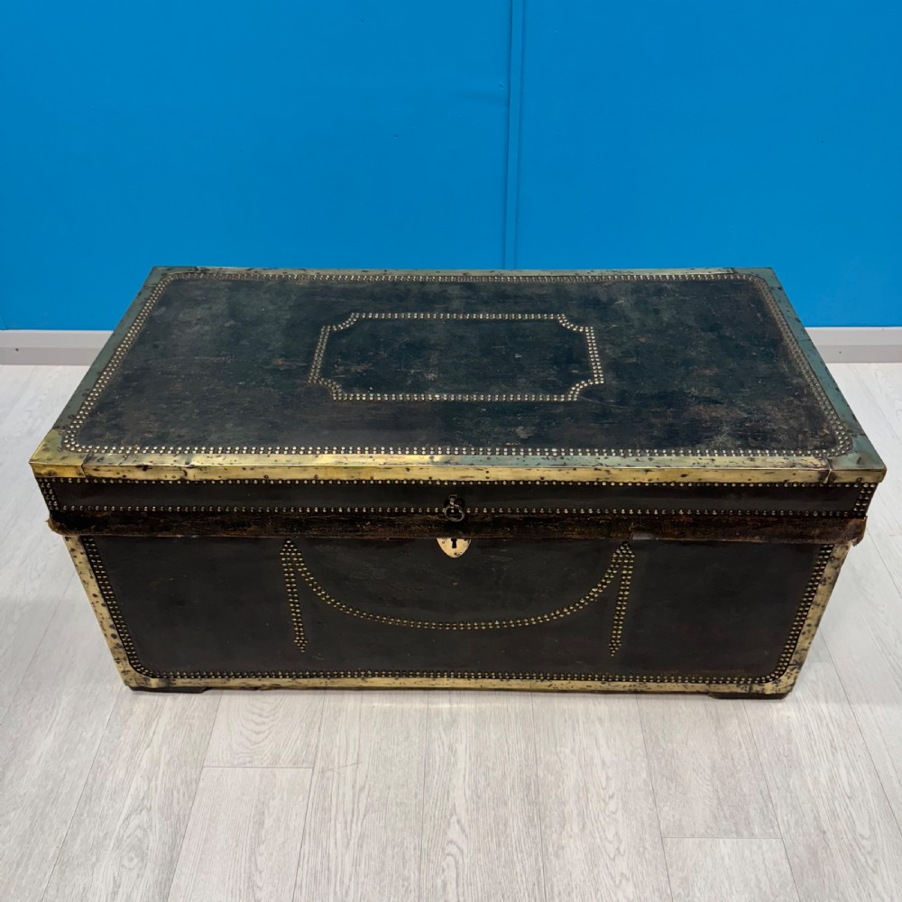 A 19th-century dark leather storage trunk featuring brass studding in geometric patterns, corner brackets, and drop handles. View V
