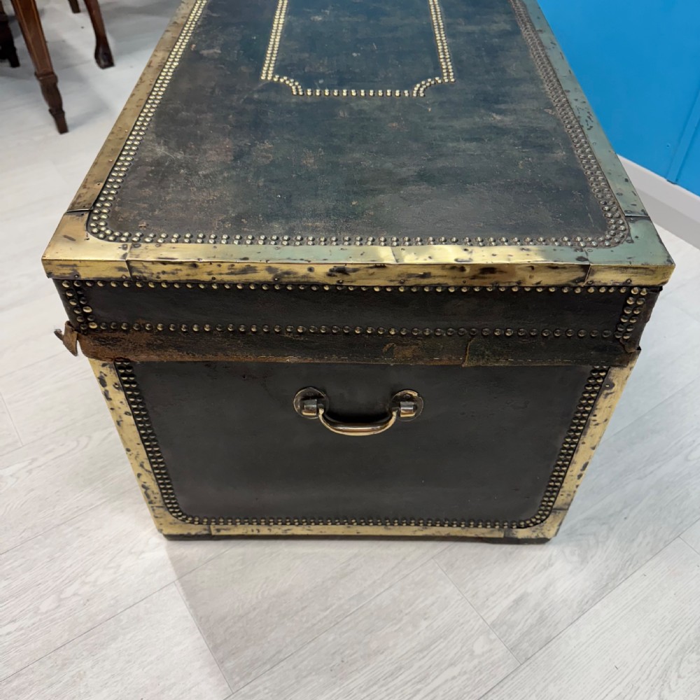 A 19th-century dark leather storage trunk featuring brass studding in geometric patterns, corner brackets, and drop handles. View VI