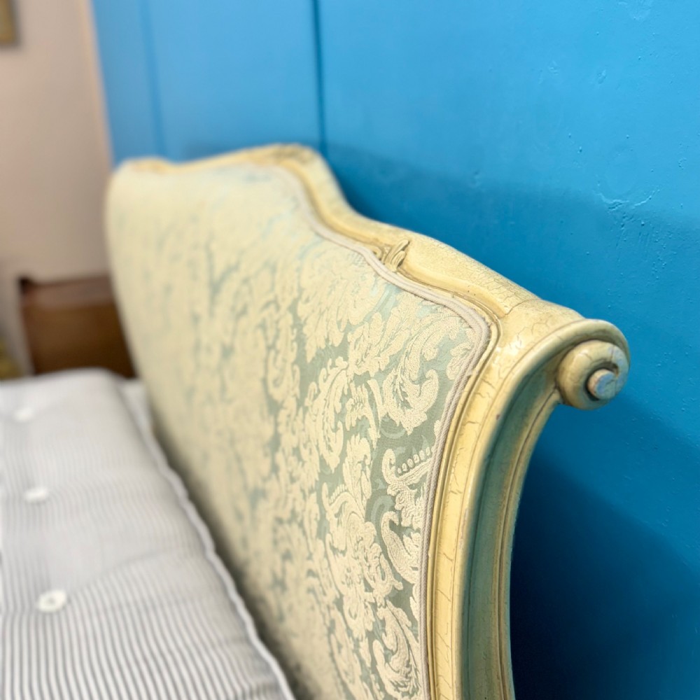 A king-size French bed frame featuring a carved cream-painted timber frame upholstered in green damask fabric with a scroll-end footboard. View X