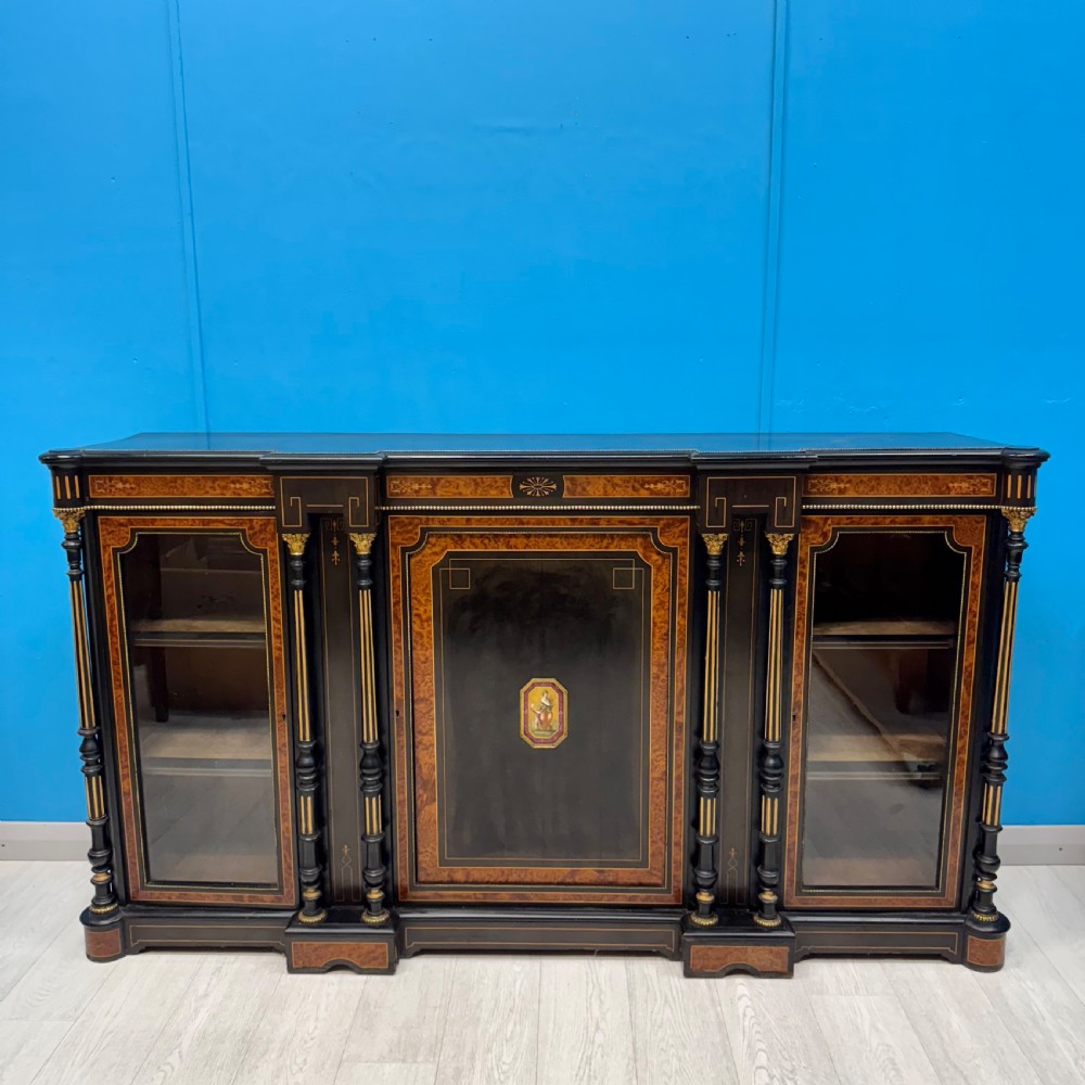 A Victorian ebonised credenza featuring a central inlaid panel door flanked by two glazed display compartments with brass mounts and fluted column details.