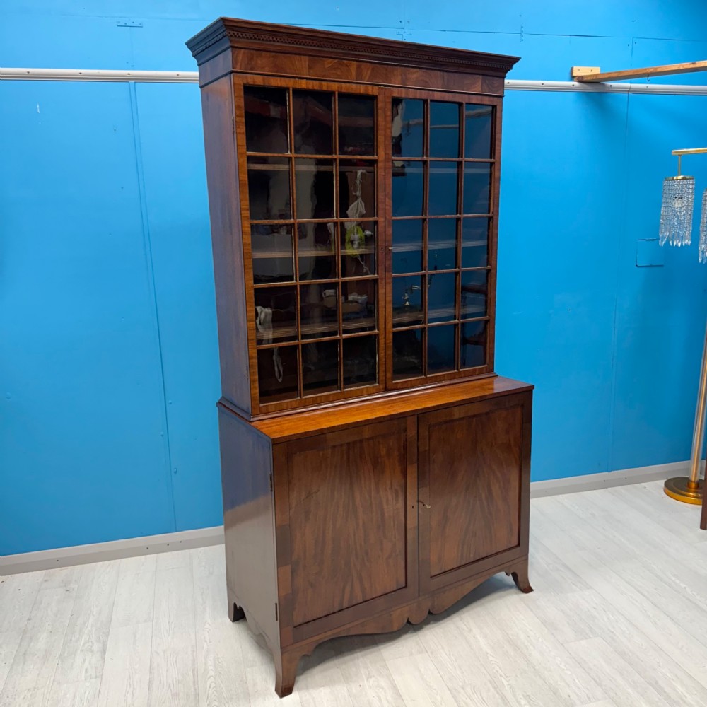 An antique Regency flame mahogany two-part bookcase featuring a glazed upper section with astragal bars and a double cupboard base.