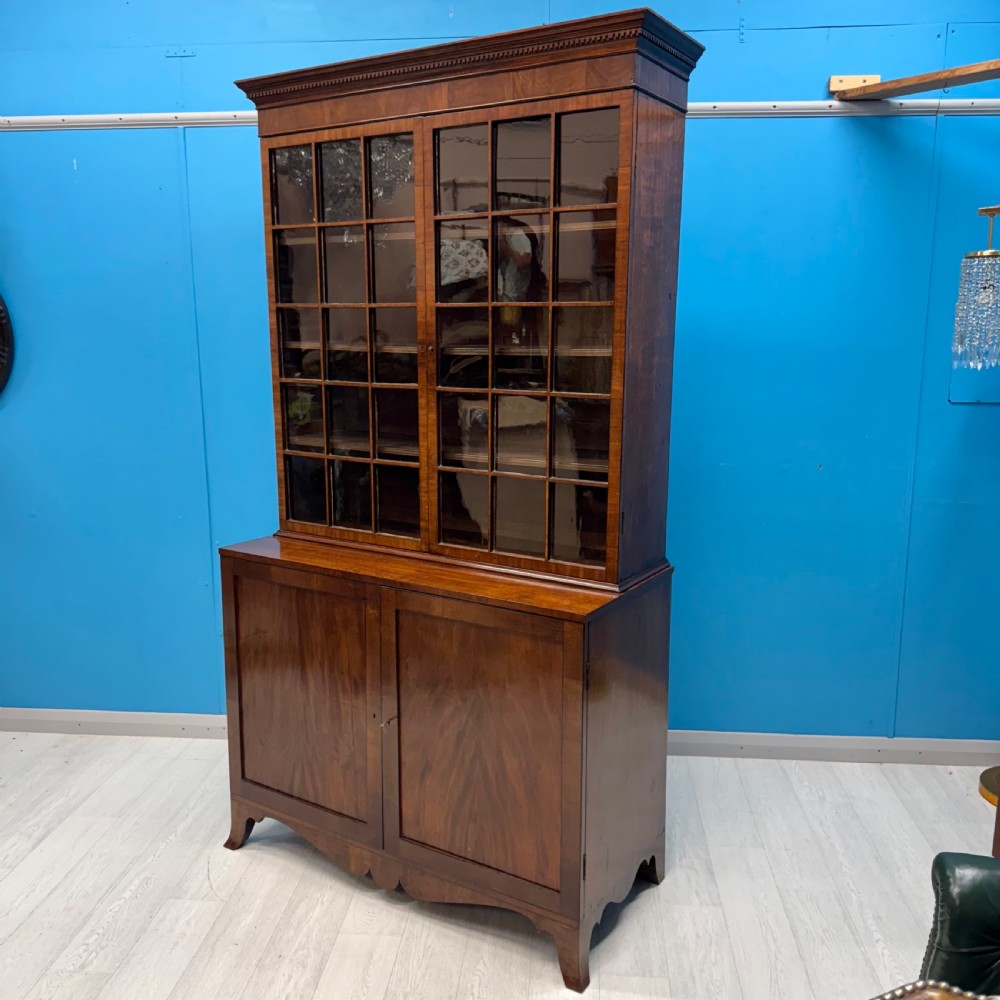 An antique Regency flame mahogany two-part bookcase featuring a glazed upper section with astragal bars and a double cupboard base. View V