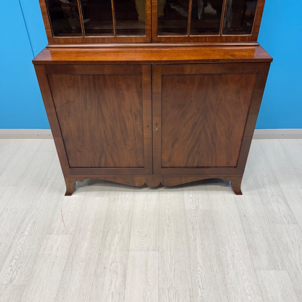 An antique Regency flame mahogany two-part bookcase featuring a glazed upper section with astragal bars and a double cupboard base. View VII