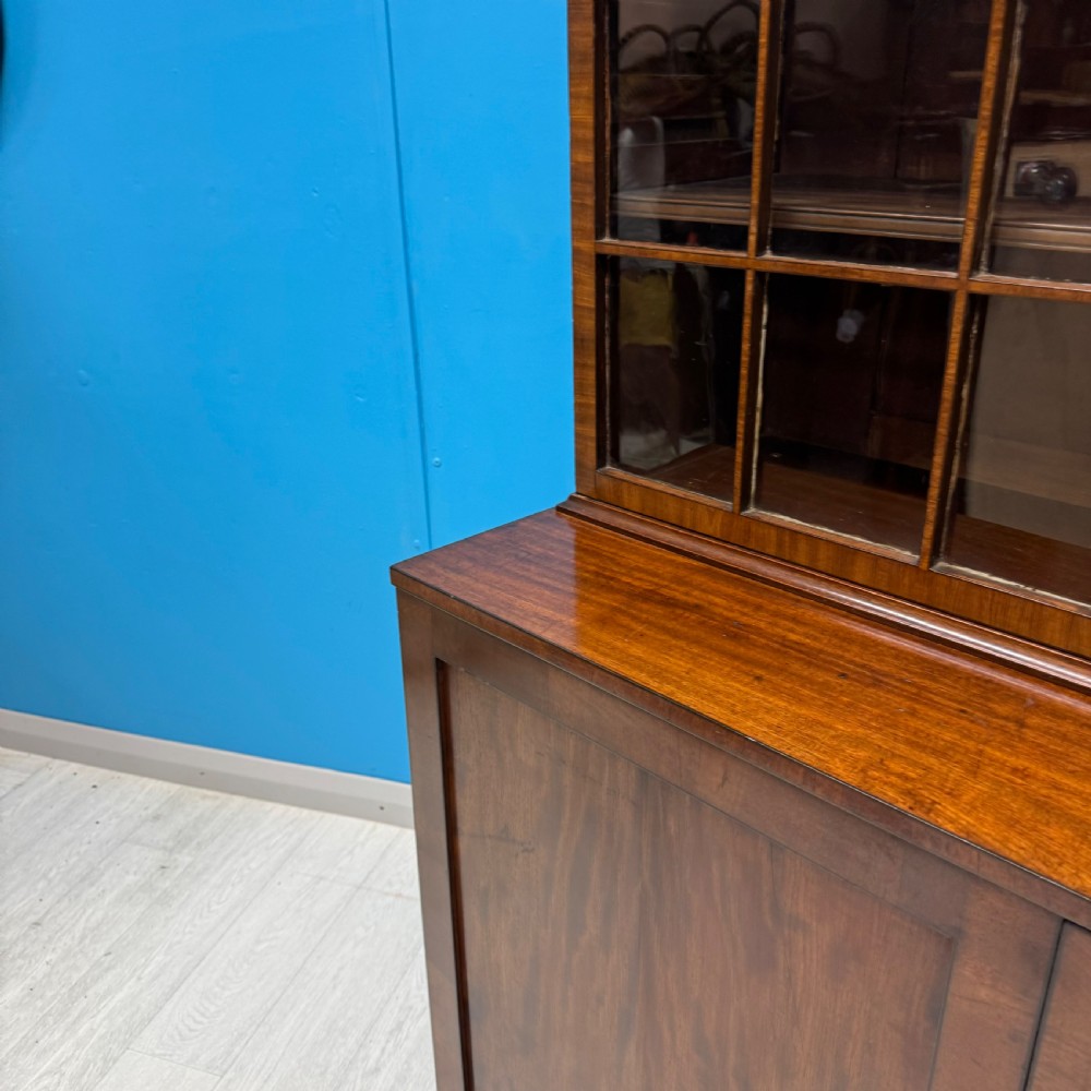 An antique Regency flame mahogany two-part bookcase featuring a glazed upper section with astragal bars and a double cupboard base. View XI