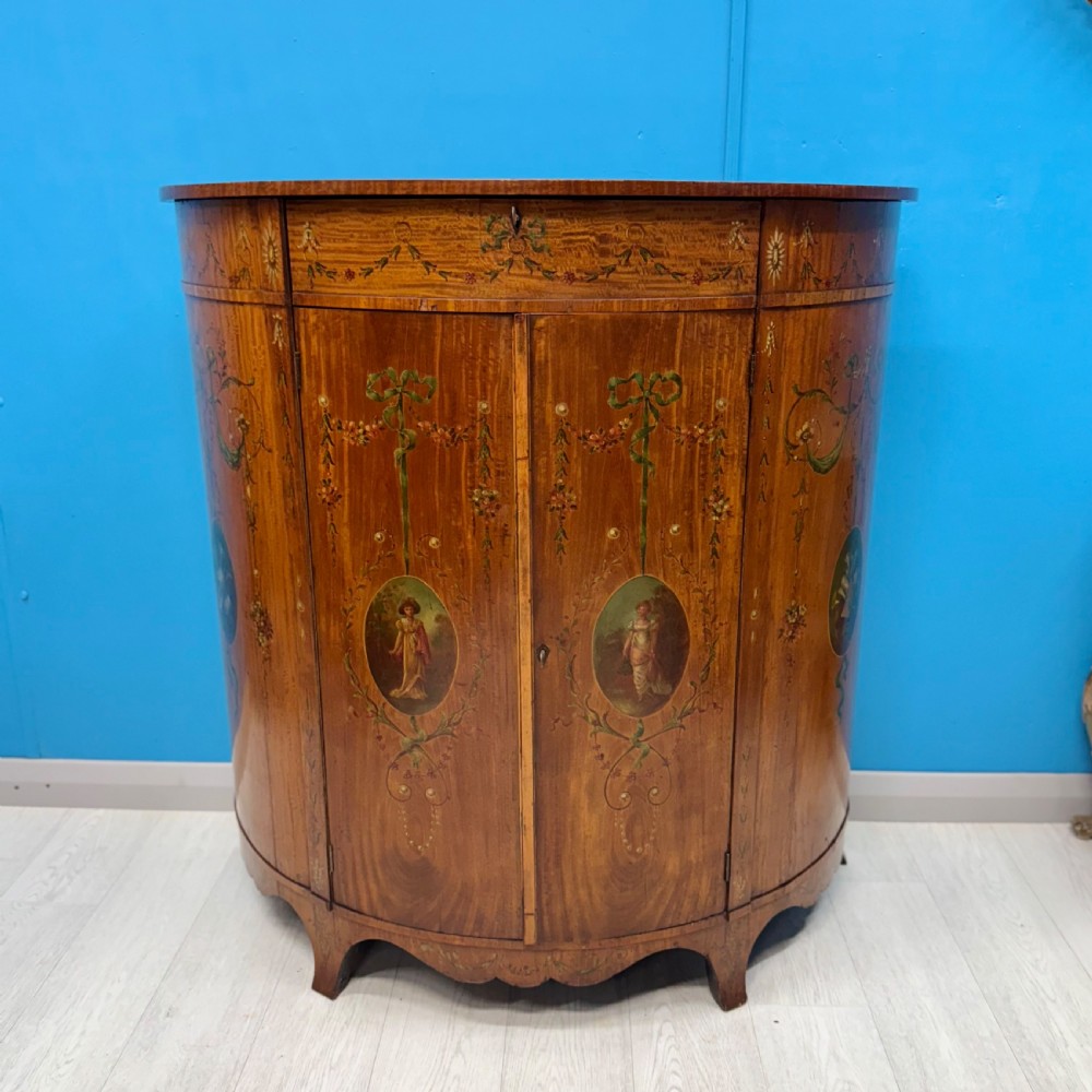 A 19th-century demi-lune satinwood side cabinet featuring hand-painted floral swags, ribbon motifs, and portrait medallions across its curved front doors. View II