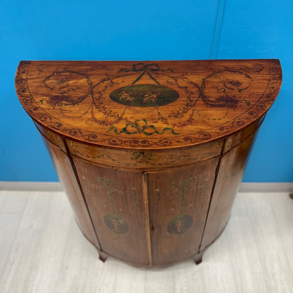 A 19th-century demi-lune satinwood side cabinet featuring hand-painted floral swags, ribbon motifs, and portrait medallions across its curved front doors. View III