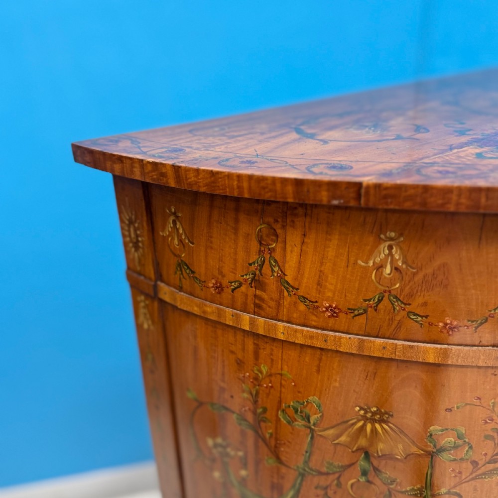 A 19th-century demi-lune satinwood side cabinet featuring hand-painted floral swags, ribbon motifs, and portrait medallions across its curved front doors. View VI