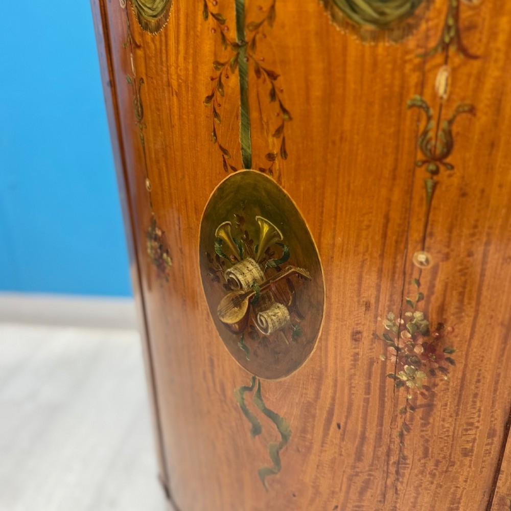 A 19th-century demi-lune satinwood side cabinet featuring hand-painted floral swags, ribbon motifs, and portrait medallions across its curved front doors. View VII