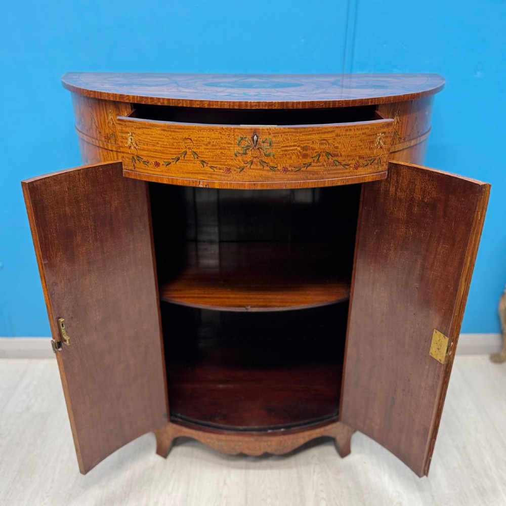 A 19th-century demi-lune satinwood side cabinet featuring hand-painted floral swags, ribbon motifs, and portrait medallions across its curved front doors. View IX