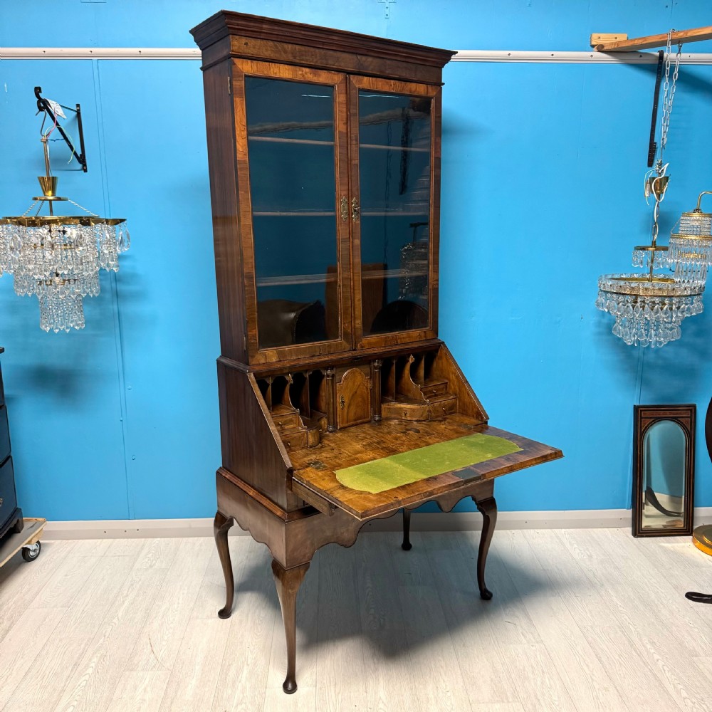 A George II walnut bureau bookcase on stand featuring a two-door glazed upper display cabinet and a slant-front writing desk over cabriole legs.