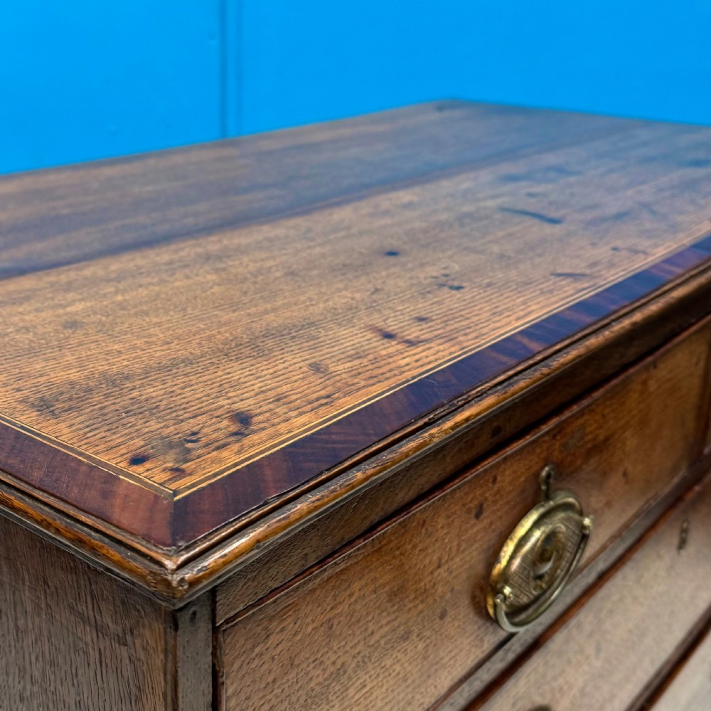 A Georgian oak chest of drawers featuring two short drawers over three long drawers with oval brass drop handles and bracket feet. View II