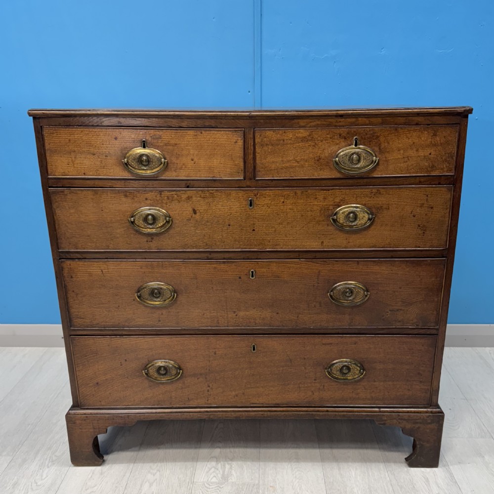 A Georgian oak chest of drawers featuring two short drawers over three long drawers with oval brass drop handles and bracket feet. View III