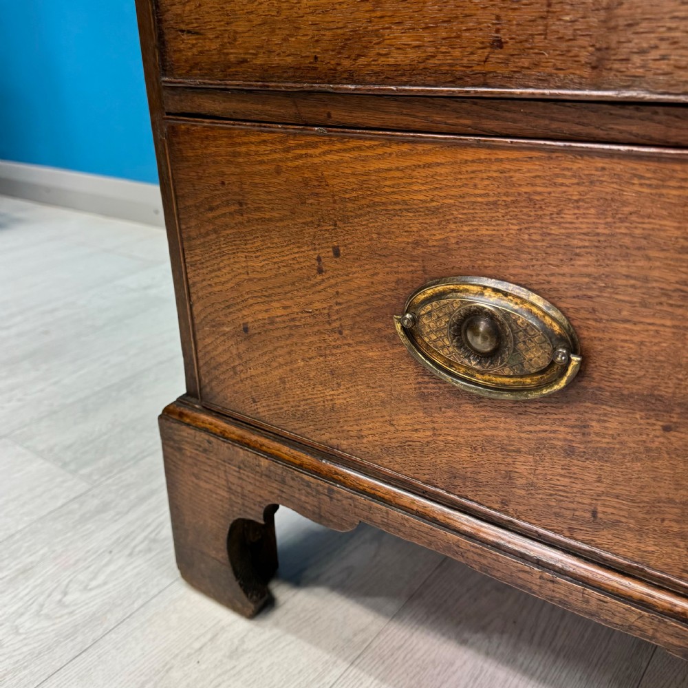 A Georgian oak chest of drawers featuring two short drawers over three long drawers with oval brass drop handles and bracket feet. View VI
