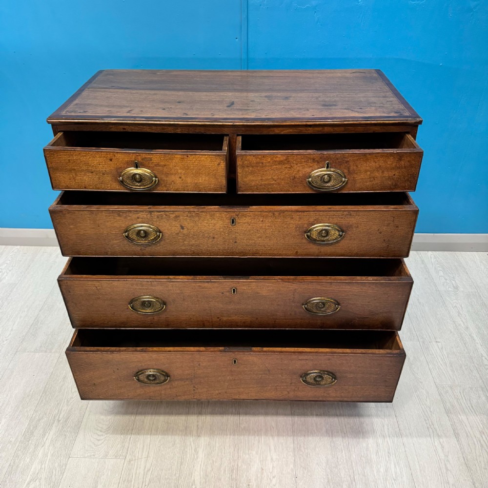 A Georgian oak chest of drawers featuring two short drawers over three long drawers with oval brass drop handles and bracket feet. View VII